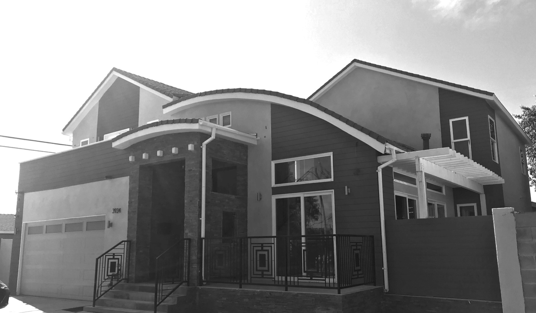 Black-and-white photograph of a completed two-story single-family house with a curved roof over the entry porch, seen from the street.